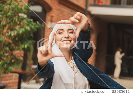 Portrait of young muslim girl making a camera frame with fingers outdoors. 82985611