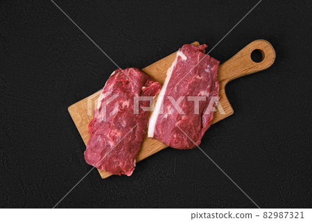 Overhead view of fresh lamb or veal steak on wooden cutting board Overhead view of fresh lamb or veal steak on wooden cutting board 82987321