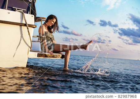 Girl sits on the edge of the yacht with legs splashing in sea water 82987968