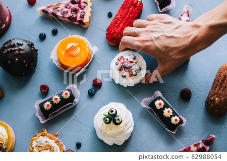 Hands taking cake from table with many different desserts. Hands taking cake from table with many different desserts. 82988054
