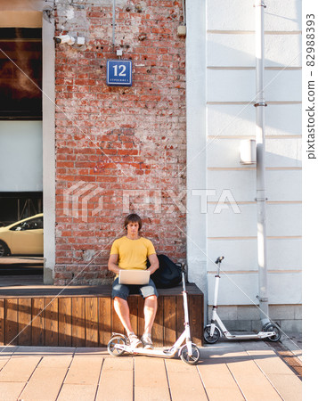 Man sits with laptop on wooden bench in street cafe. Freelancer at work. Student learns remotely from outdoors. Modern lifestyle. Summer vibes. Open air workplace. Man sits with laptop on wooden bench in street cafe. Freelancer at work. Student learns remotely from outdoors. Modern lifestyle. Summer vibes. Open air workplace. 82988393