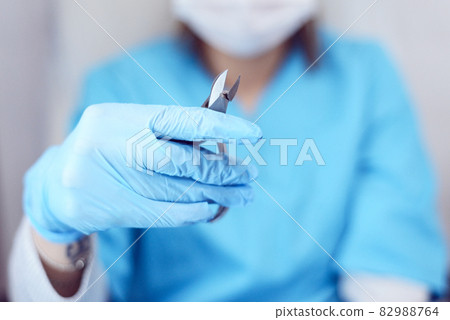 A girl in a mask and a medical gown with cuticle nippers in her hands, a salon worker, a manicure and pedicure master 82988764