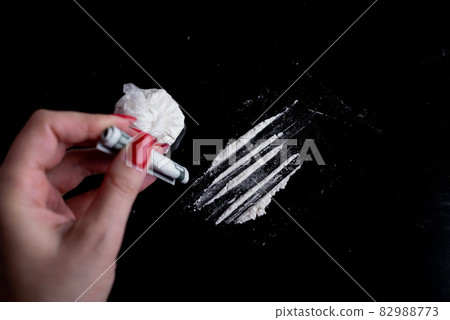 white powder (heroin, cocaine, narcotic) in a plastic bag on a black background, drugs are scattered in the form of a path, a hand with a bill folded into a tube 82988773