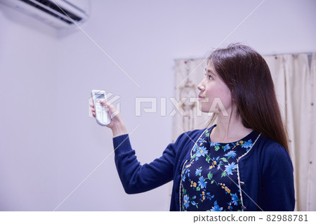 Japanese woman adjusting the air conditioner with a remote control Japanese woman adjusting the air conditioner with a remote control 82988781
