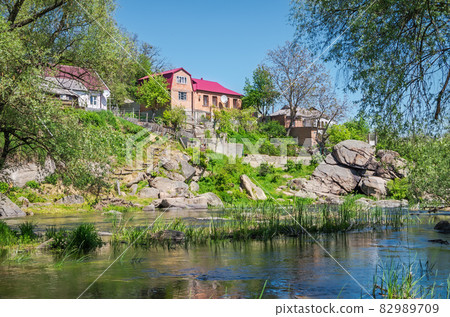 River with stony bank flows through village 82989709