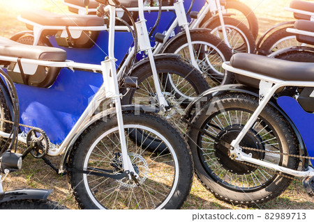 Many retro fat electric bicycle scooters parked on dirt grass field outdoor ready for hire rental sharing cpuntry parl leisure recreation trip. E power transport rent equipment. Rural offroad cycling Many retro fat electric bicycle scooters parked on dirt grass field outdoor ready for hire rental sharing cpuntry parl leisure recreation trip. E power transport rent equipment. Rural offroad cycling 82989713