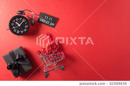 Online shopping of China, 11.11 singles day sale concept. Top view of shopping cart, black christmas gift boxes with sale card on red background with copy space. Online shopping of China, 11.11 singles day sale concept. Top view of shopping cart, black christmas gift boxes with sale card on red background with copy space. 82989836