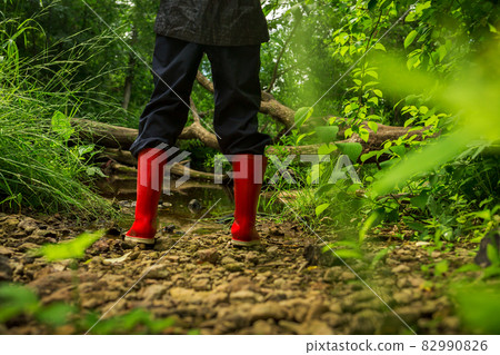A child in red rubber boots on the shore of a forest river 82990826