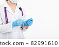 A young nurse in a mask opens a syringe on a white background in a white coat, to make a vaccination 82991610