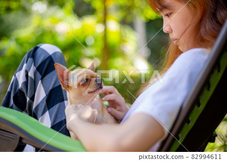 Happy asian woman sitting with a chihuahua dog on a foldable chair. 82994611