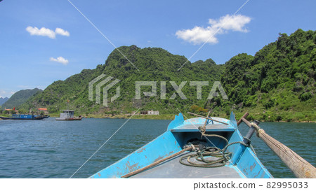 Looking at the blue river and high mountain from the bow of a small wooden boat in Phong Nha - Ke Bang National Park, Ninh Binh Province, Vietnam Looking at the blue river and high mountain from the bow of a small wooden boat in Phong Nha - Ke Bang National Park, Ninh Binh Province, Vietnam 82995033