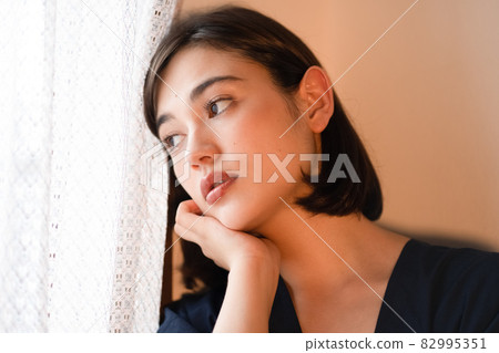 Portrait of a woman standing by the window at dusk Portrait of a woman standing by the window at dusk 82995351