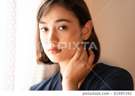 Portrait of a woman standing by the window at dusk Portrait of a woman standing by the window at dusk 82995392