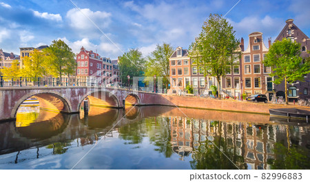Amsterdam. Panoramic view of the historic city center of Amsterdam. Traditional houses and bridges of Amsterdam. An early quiet morning and the serene reflection of houses in the water. A European Amsterdam. Panoramic view of the historic city center of Amsterdam. Traditional houses and bridges of Amsterdam. An early quiet morning and the serene reflection of houses in the water. A European 82996883