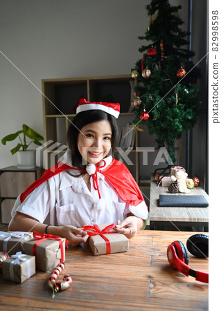 Happy woman decorating Christmas Gift and smiling to camera. 82998598