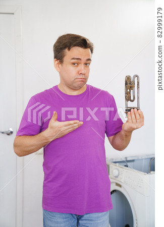 sad repairman of washing machine holds old tubular electric heater  sad repairman of washing machine holds old tubular electric heater  82999179