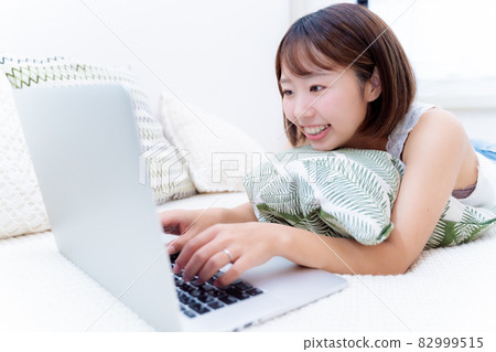一個微笑的女人臉朝下躺著操作電腦 82999515