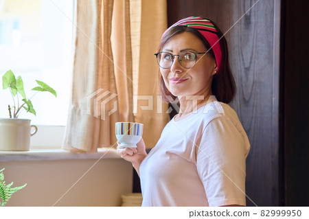 Portrait of a middle aged woman at home in the kitchen with a cup of coffee 82999950