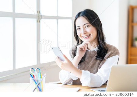 A woman who manipulates a smartphone in the living room A woman who manipulates a smartphone in the living room 83000314