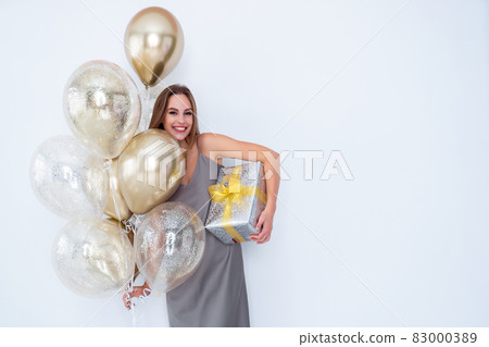 Photo of smiling girl holds large wrapped giftbox and many air balloons. came to party. Celebration  83000389
