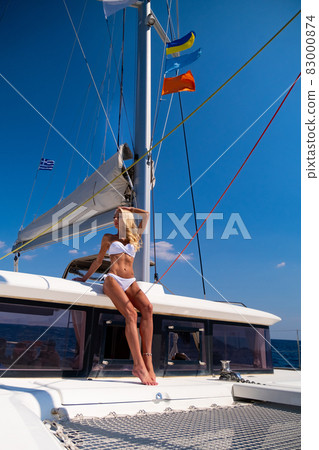 Woman in bikini tanning and relaxing drinking wine on a summer catamaran sailing cruise Woman in bikini tanning and relaxing drinking wine on a summer catamaran sailing cruise 83000874