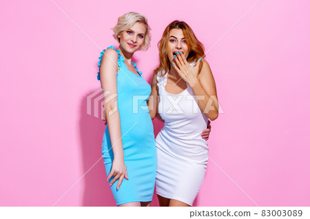 Two stunning beautiful confident lady chic hugging wearing pretty nice cute dresses isolated on pink studio background 83003089