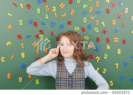 Girl stands in front of a green school board with magnets of numbers that depict her thoughts 83003973