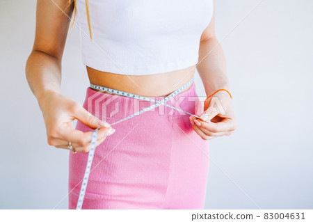 Slim woman measuring her waist's size with tape measure on white background. Successful weight loss. Slim fit concept. Slim woman measuring her waist's size with tape measure on white background. Successful weight loss. Slim fit concept. 83004631