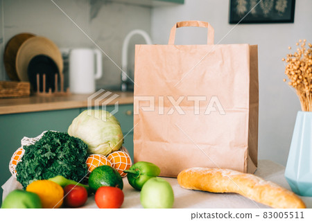 Eco shopping paper bag with fresh vegetables and baguette on the table in modern kitchen. Food delivery or market shopping concept.. Eco shopping paper bag with fresh vegetables and baguette on the table in modern kitchen. Food delivery or market shopping concept.. 83005511