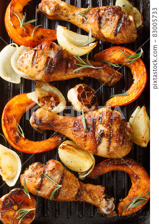 Black grill background with fried chicken legs, pumpkin slices, onions and garlic close-up. vertical top view Black grill background with fried chicken legs, pumpkin slices, onions and garlic close-up. vertical top view 83005733