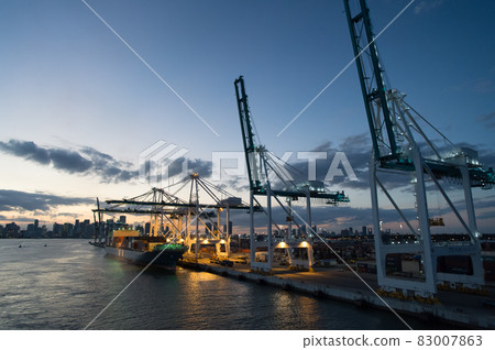 Miami, USA - March 01, 2016: freight carrier and cranes on evening sky. Cargo carrier on pier side. City skyline at dusk. Shipping and shipment. Cargo loading 83007863