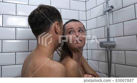 Reconciliation under shower couple after quarrel closeup. Sad woman in tears hugs her boyfriend in bathroom. Man comes up and hugs resentful girl accepting apology. Reconciliation concept. Slow motion 83007887