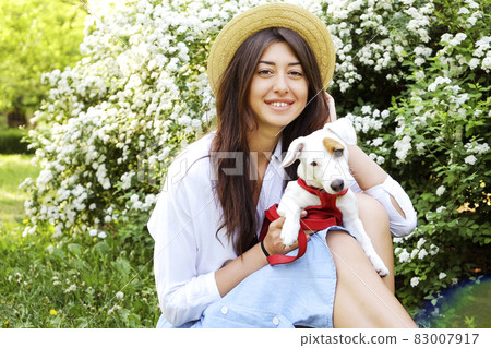 Attractive hipster young woman went for a walk in the park, playing with cute jack russell terrier puppy on clear sunny day. 83007917