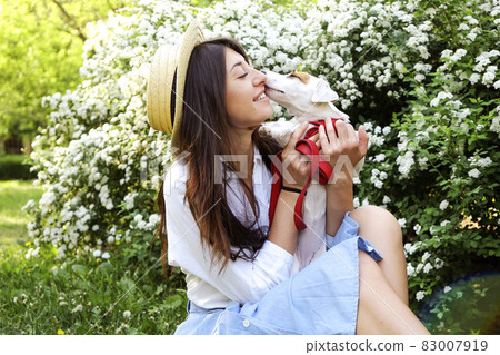 Attractive hipster young woman went for a walk in the park, playing with cute jack russell terrier puppy on clear sunny day. 83007919