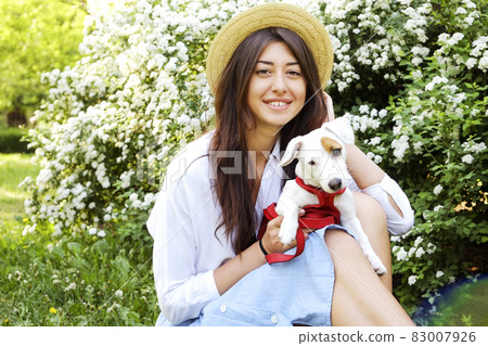 Attractive hipster young woman went for a walk in the park, playing with cute jack russell terrier puppy on clear sunny day. 83007926