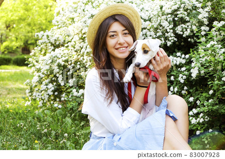 Attractive hipster young woman went for a walk in the park, playing with cute jack russell terrier puppy on clear sunny day. 83007928