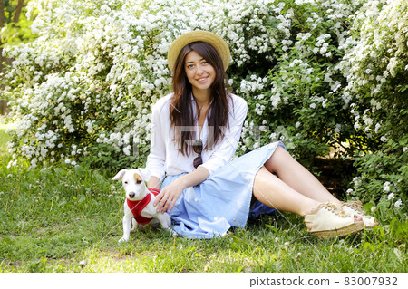 Attractive hipster young woman went for a walk in the park, playing with cute jack russell terrier puppy on clear sunny day. 83007932