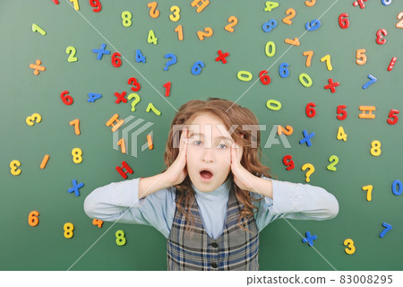 Girl stands in front of a green school board with magnets of numbers that depict her thoughts Girl stands in front of a green school board with magnets of numbers that depict her thoughts 83008295
