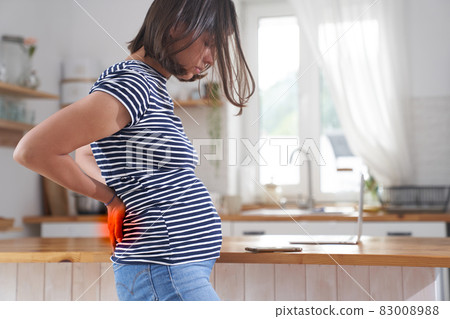 A young pregnant woman holds her back with her hands. A brunette in the third trimester of pregnancy. The concept of back pain during pregnancy. High quality photo 83008988