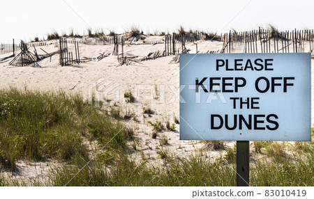 Keep off the dunes sign in front of sand dunes with broken fences on Fire Island Keep off the dunes sign in front of sand dunes with broken fences on Fire Island 83010419