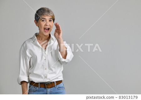 Middle aged Asian woman is holding hand near mouth and telling a secret isolated on white background 83013179