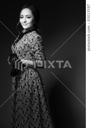 A girl standing in a blue dress in the style of the 1900s, in a retro dress, hat and with a bouquet of flowers on a gray background. Historical fashion of the 19th century. High quality photo A girl standing in a blue dress in the style of the 1900s, in a retro dress, hat and with a bouquet of flowers on a gray background. Historical fashion of the 19th century. High quality photo 83013597