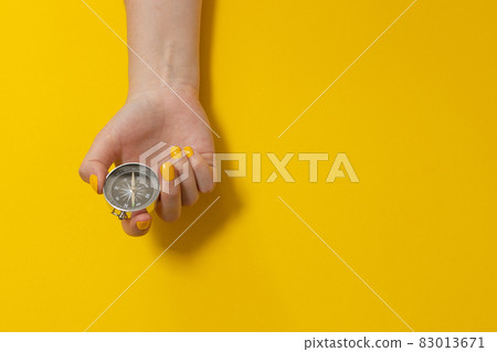 Tourist hand holding a compass on a yellow background with copy space. Journey, adventure lifestyle. Road to home. Trip. 83013671
