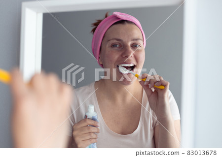 Young beautiful woman with toothbrush near mirror in bathroom. Oral hygiene and teeth care 83013678