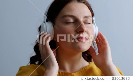 Close up portrait of stylish young girl listening to music with closed eyes and enjoying melody on gray background 83013683