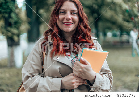 Young caucasian female student with books outside near campus in nature park 83013773
