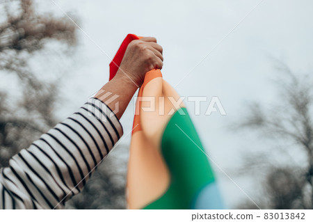 Person hand with a colorful rainbow flag on blue background. LGBT equal rights movement and gender equality concept Person hand with a colorful rainbow flag on blue background. LGBT equal rights movement and gender equality concept 83013842