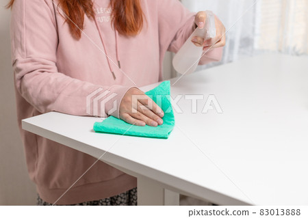 Close up of cleaning white table, sanitizing table surface with disinfectant antibacterial spray bottle, washing surfaces with towel and gloves. COVID-19 prevention sanitizing inside Close up of cleaning white table, sanitizing table surface with disinfectant antibacterial spray bottle, washing surfaces with towel and gloves. COVID-19 prevention sanitizing inside 83013888