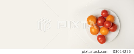 Creative layout made of various fresh red yellow tomato isolated on a white plate on grey background. Top view. Vegan 83014256