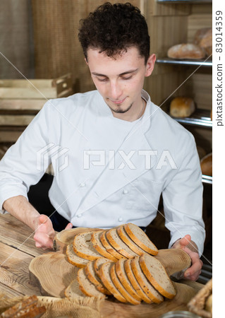 A handsome baker serves fresh bread to thirsty customers. Sale of bread in a traditional bakery store. A handsome baker serves fresh bread to thirsty customers. Sale of bread in a traditional bakery store. 83014359